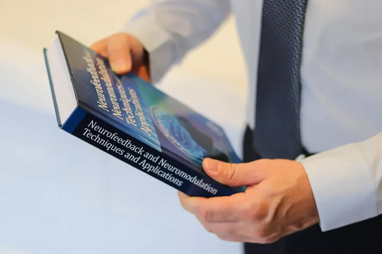 Dr. Rafael Higashi segurando um livro sobre neurofeedback e neuromodulação